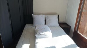 A neatly made bed with white linens and pillows, a wooden nightstand, and a window with curtains.