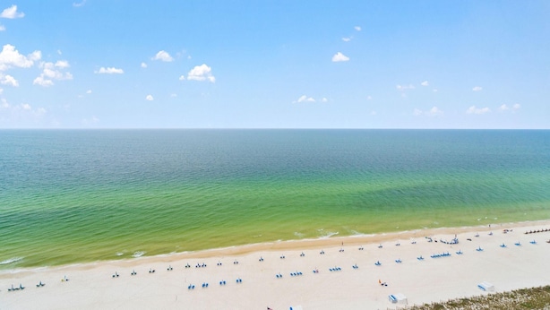 A beach with clear turquoise water, a sandy shore, and several blue umbrellas. - Indigo East 1702 (Pensacola)