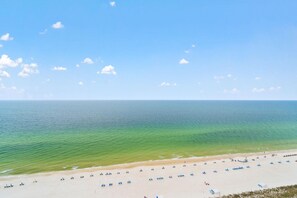 A beach with clear turquoise water, a sandy shore, and several blue umbrellas.