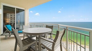 A balcony with a round table and chairs, overlooking a beach. - Indigo East 1702 (Pensacola)