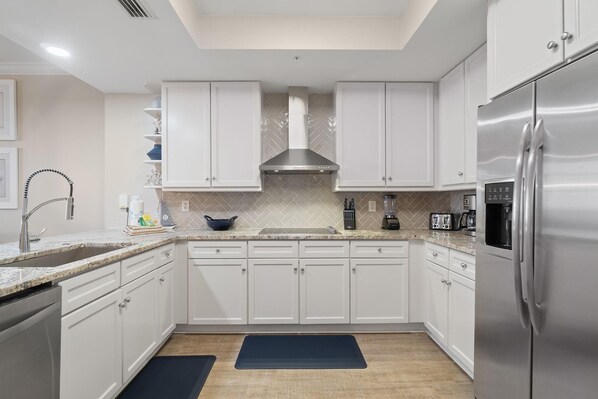 A modern kitchen with white cabinets, stainless steel appliances, and a herringbone tile backsplash.