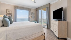 A hotel room with a bed, a TV, a dresser, and a balcony with a view. - Indigo East 1702 (Pensacola)