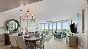 A spacious living area with a dining table, chairs, a chandelier, a large mirror, artwork, and a television. - Caribe D411 (Orange Beach)