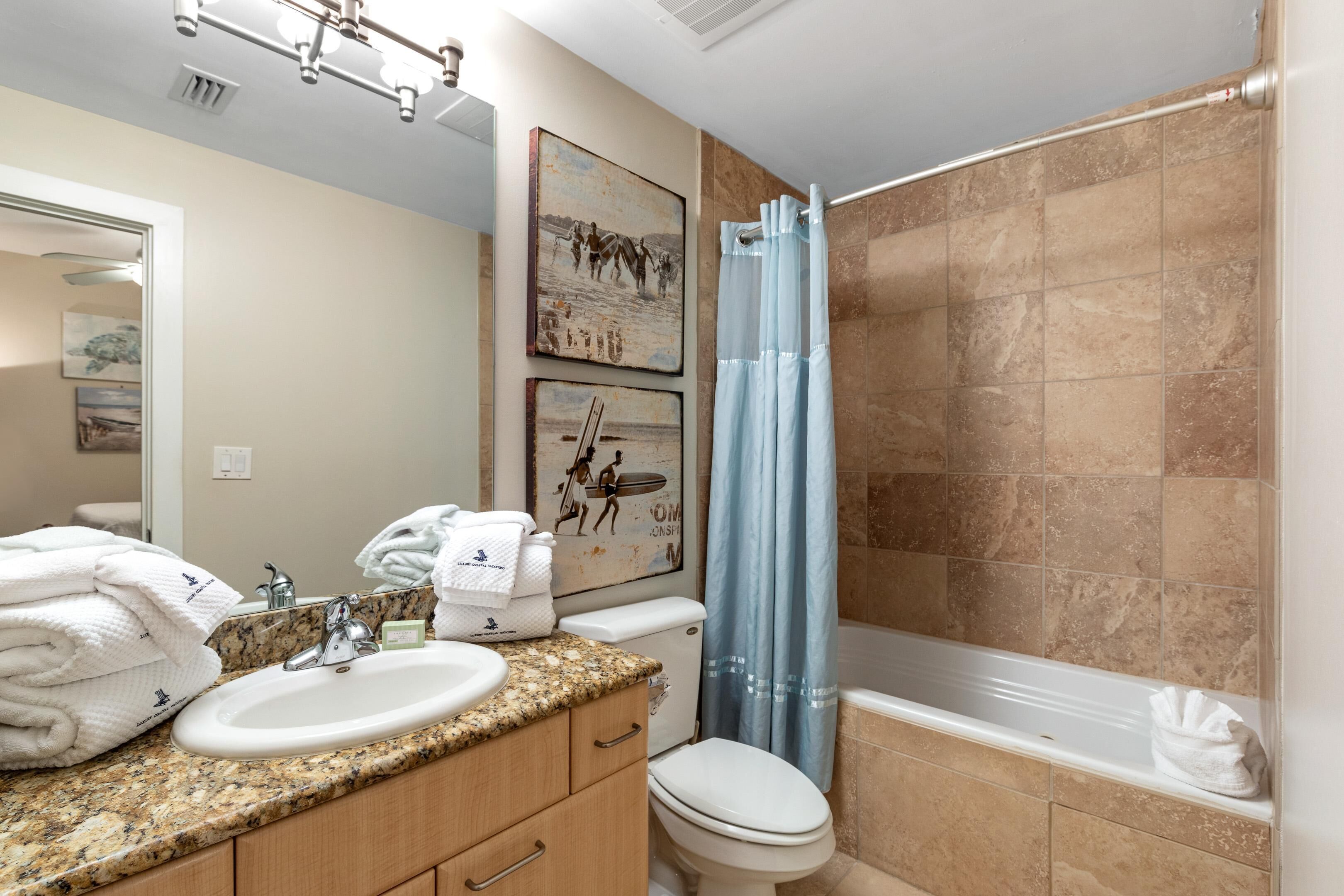 A bathroom with a sink, toilet, and bathtub. There are towels stacked on the counter, and a shower curtain is visible.