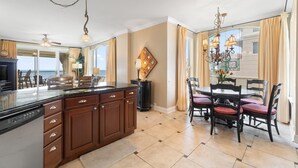 Une cuisine moderne dotée d’un grand îlot central, de meubles de rangement en bois foncé et d’un coin repas agrémenté d’un lustre.