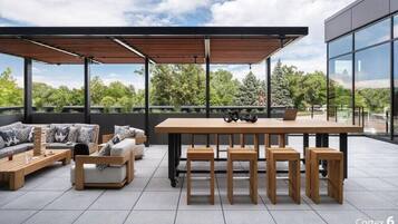 Un espacio moderno al aire libre con una mesa de madera y bancos, un sofá, y una computadora portátil sobre la mesa.