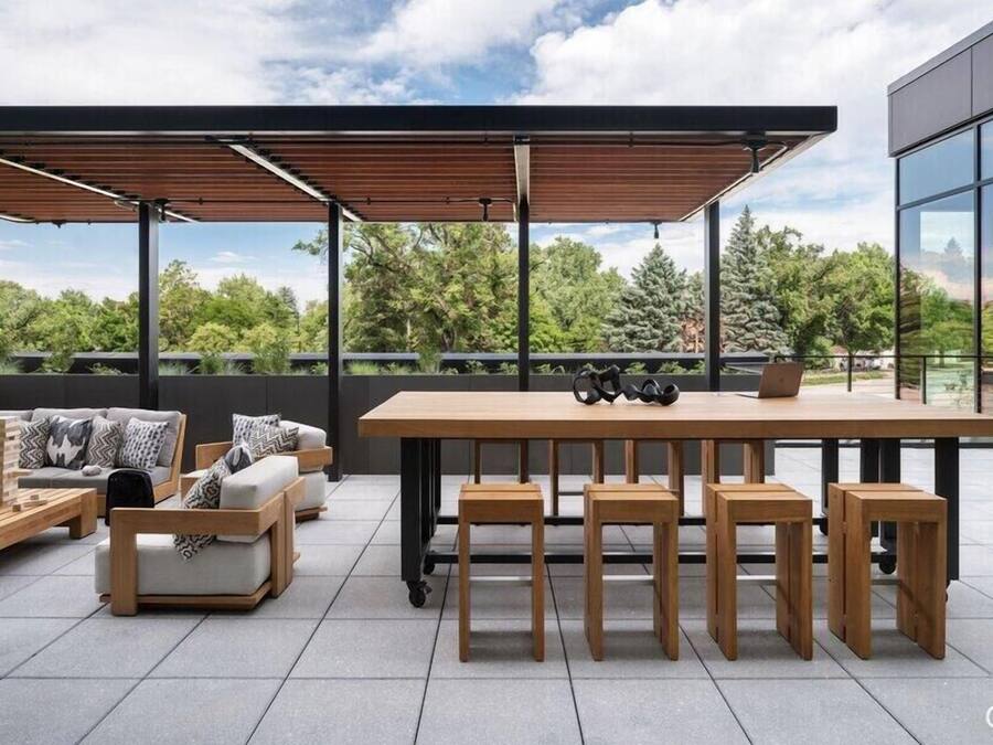 A modern outdoor seating area with a wooden table and benches, a sofa, and a laptop on the table.