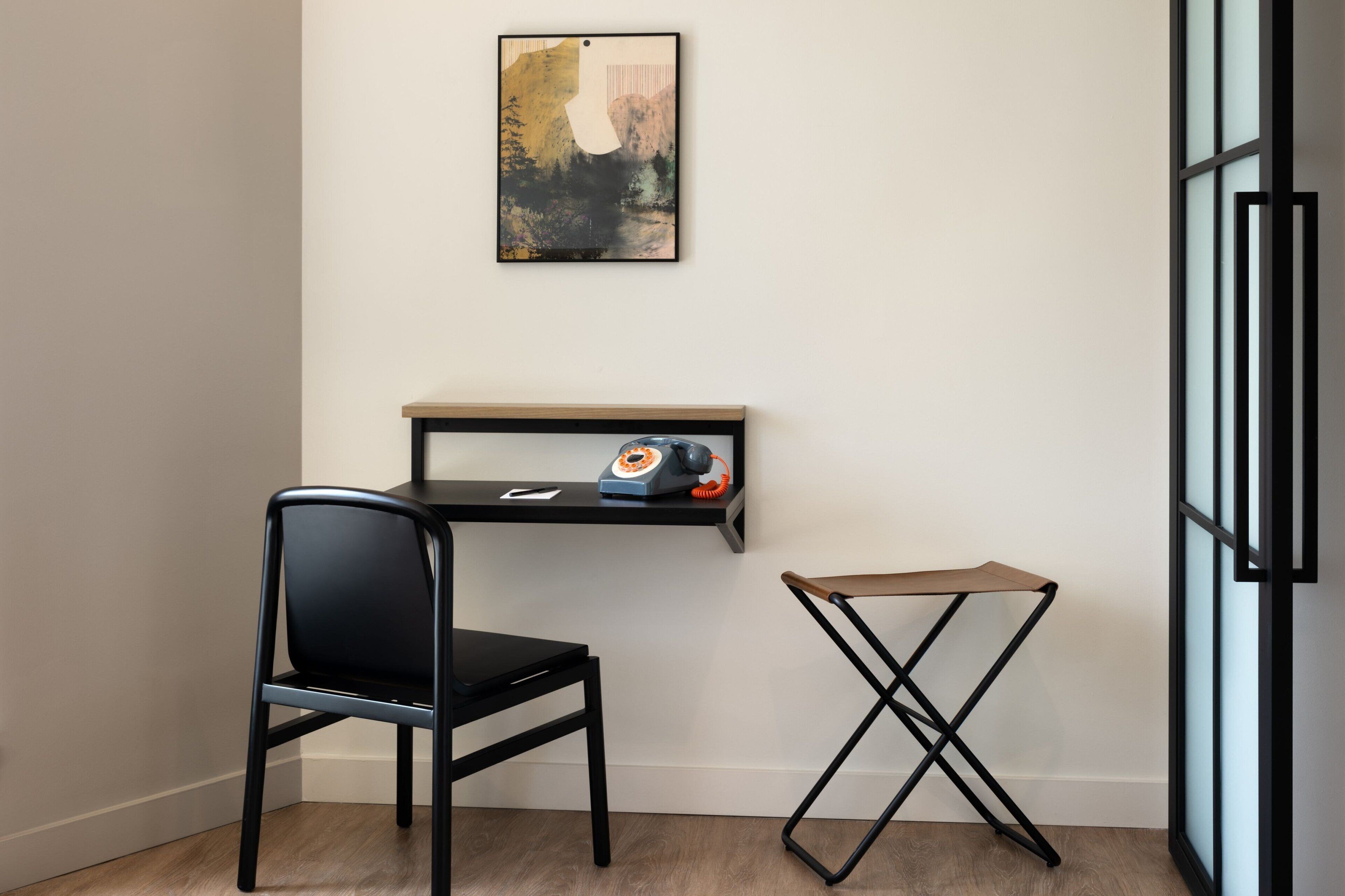 A corner room with a black chair, a small table with a telephone, and a framed picture on the wall.