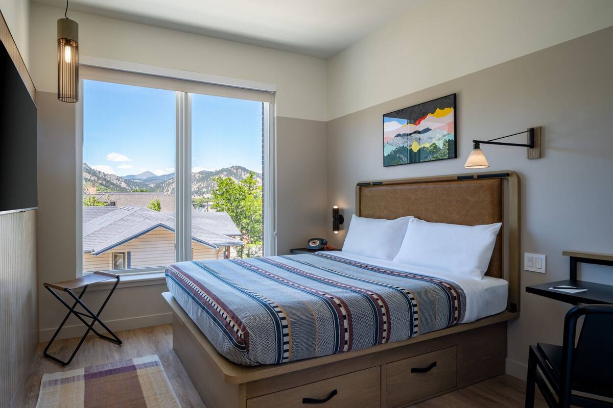 A bedroom with a bed, a desk, a chair, a nightstand, a lamp, and a painting.