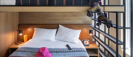 A bunk bed with a headboard, a bedside table with a lamp, a remote control, a pink hat, headphones, and roller skates.