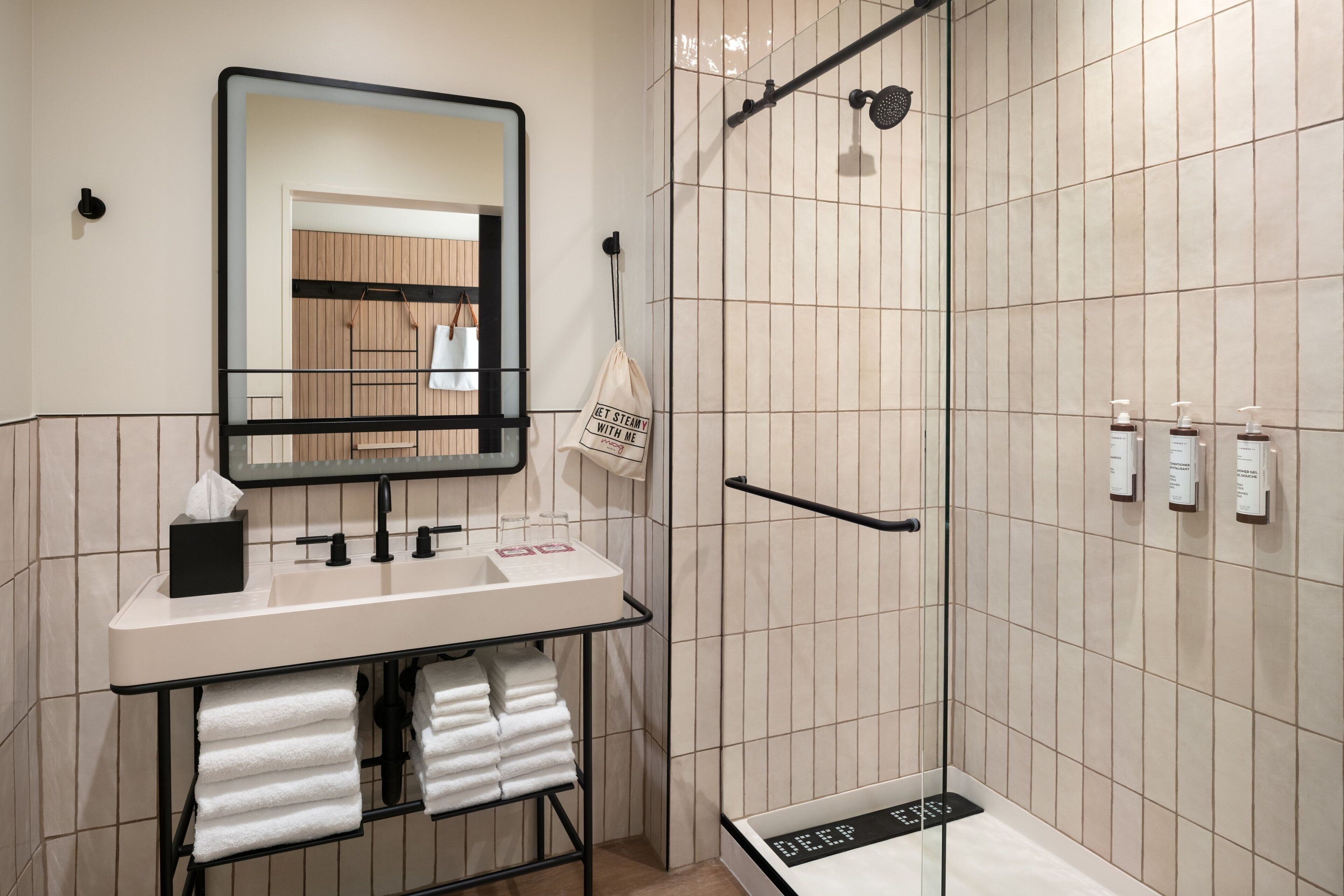 Un baño moderno con lavamanos, espejo, toallero y zona de ducha.