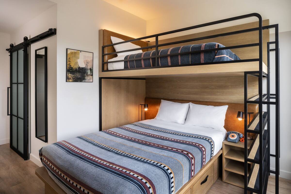 A bunk bed with a patterned bedspread, a bedside table with a lamp, and a framed picture on the wall.
