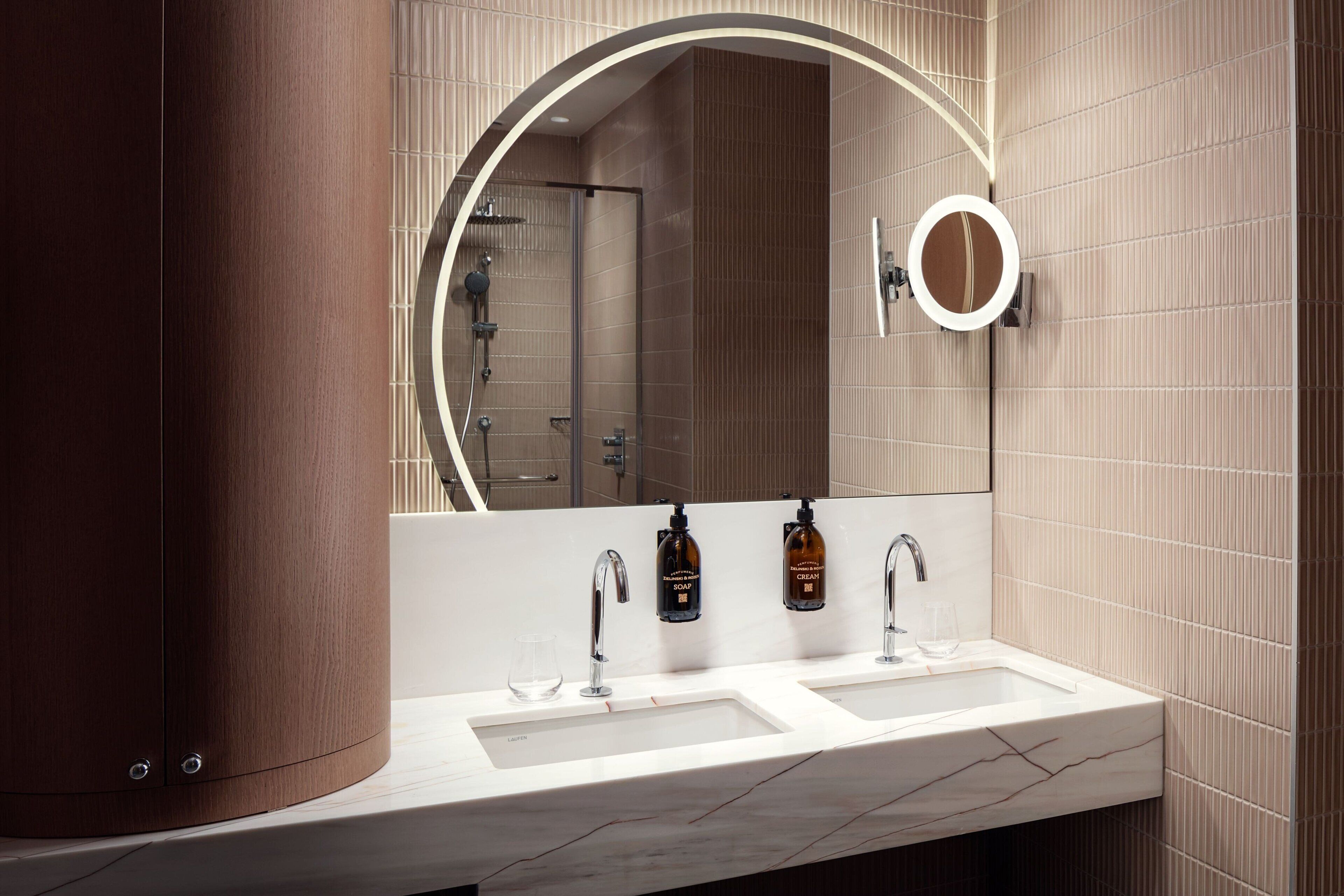 A modern bathroom with two sinks, a large mirror, and a shower area.