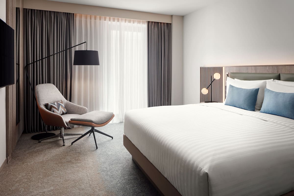 A hotel room with a large bed, a chair, a TV, and a lamp.