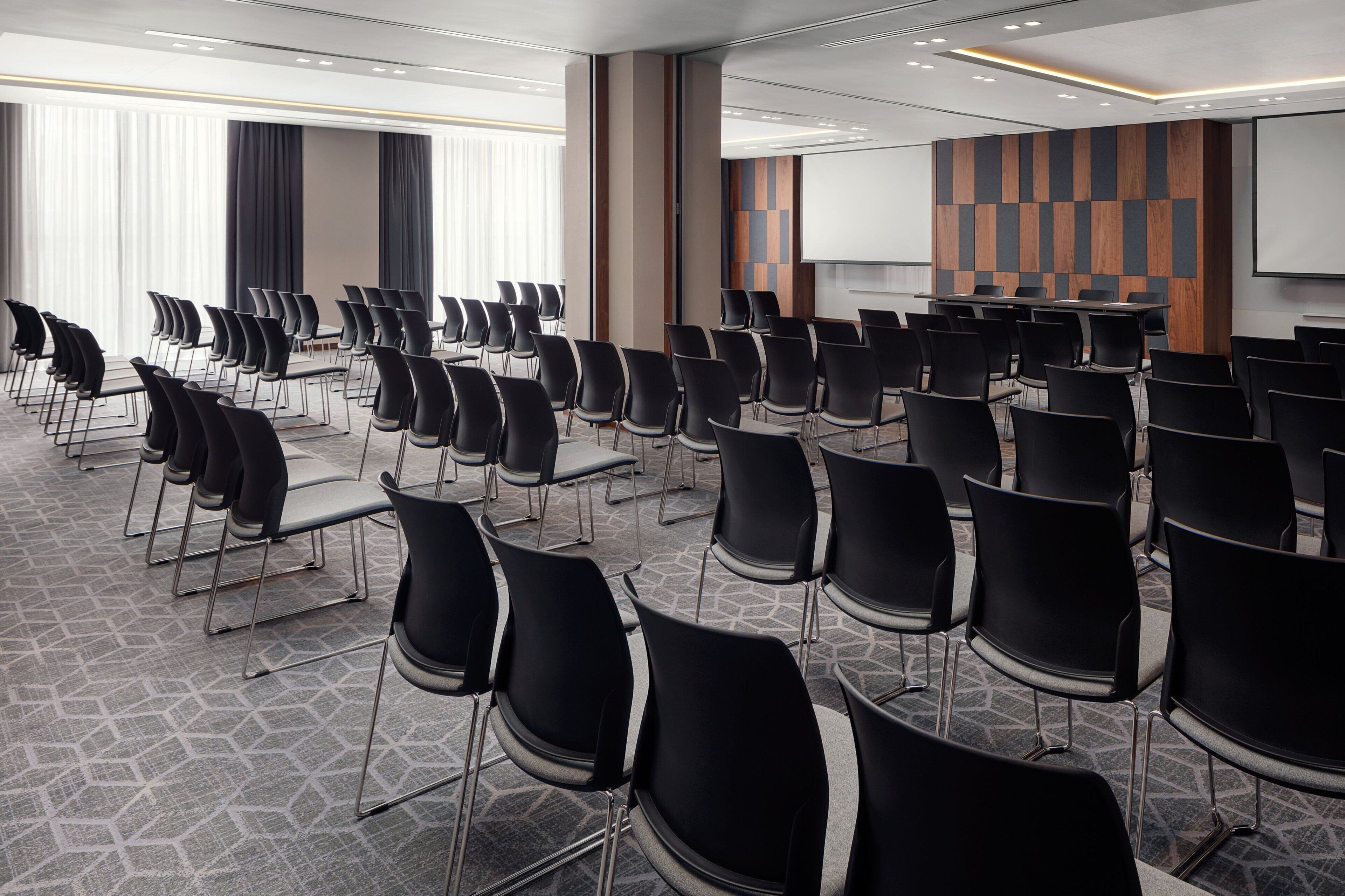 A conference room with rows of black chairs, a large table, and a projector screen.