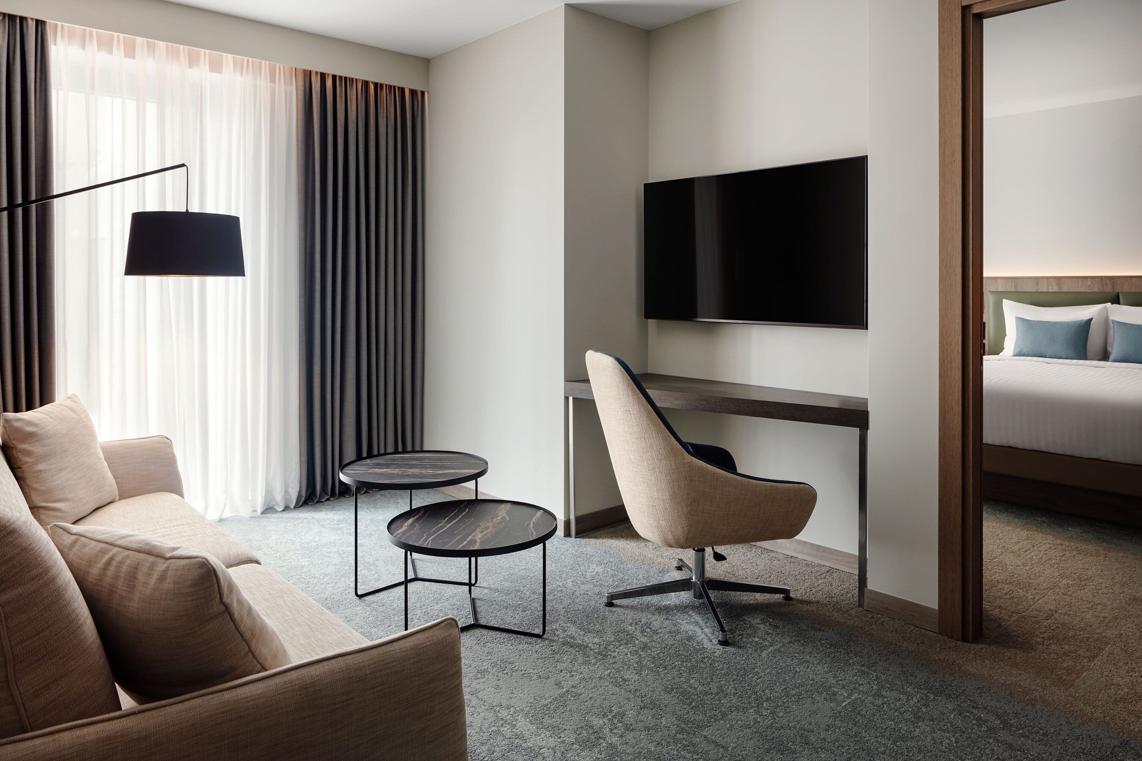 A modern hotel room with a sofa, a desk with a chair, a flat-screen TV, and a bed.
