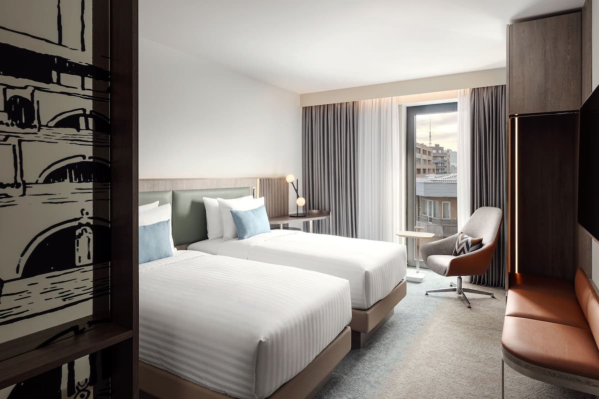 A hotel room with two beds, a desk, a chair, and a TV.
