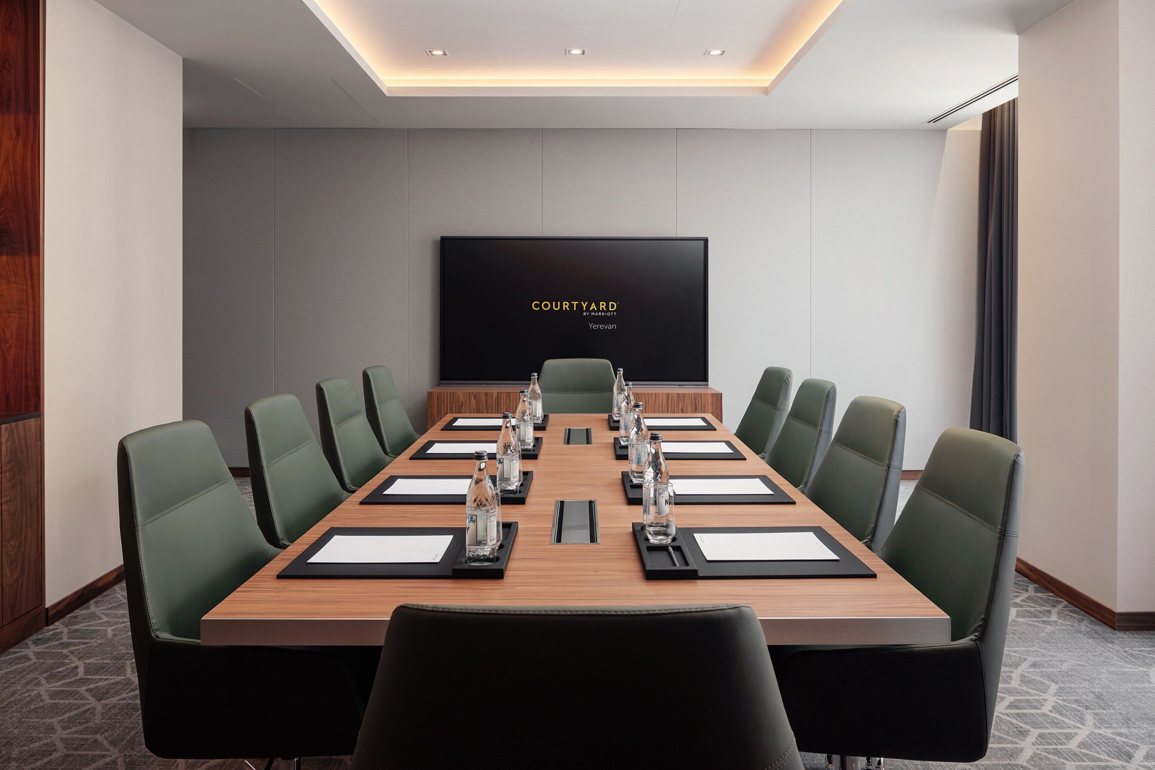 A conference room with a long table, green chairs, and a large screen displaying "COURTYARD BY YREVAAN".