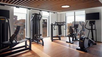 A gym with various exercise machines, large windows, and a wooden ceiling.