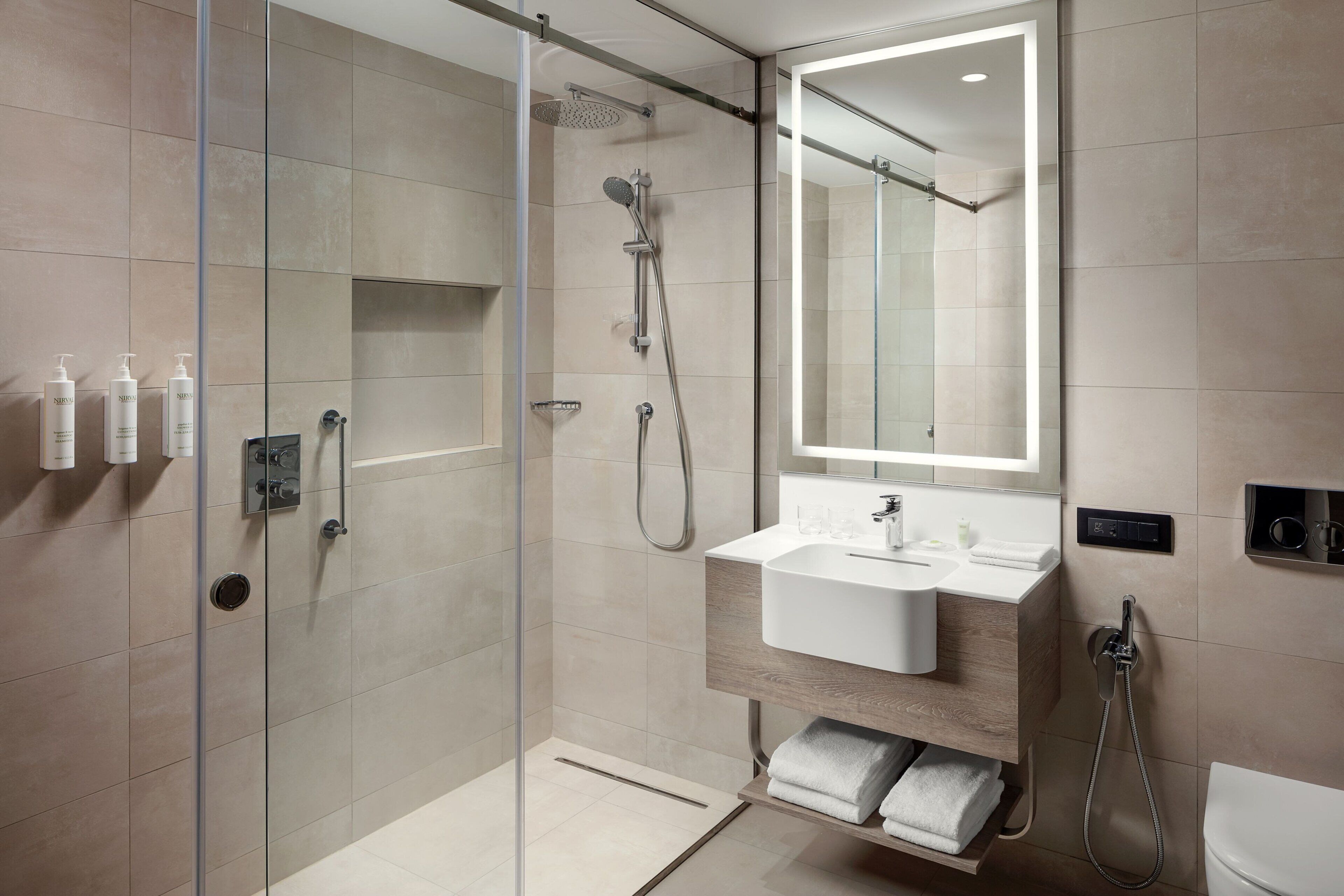 Un baño moderno con ducha de vidrio, lavamanos blanco y un espejo grande.