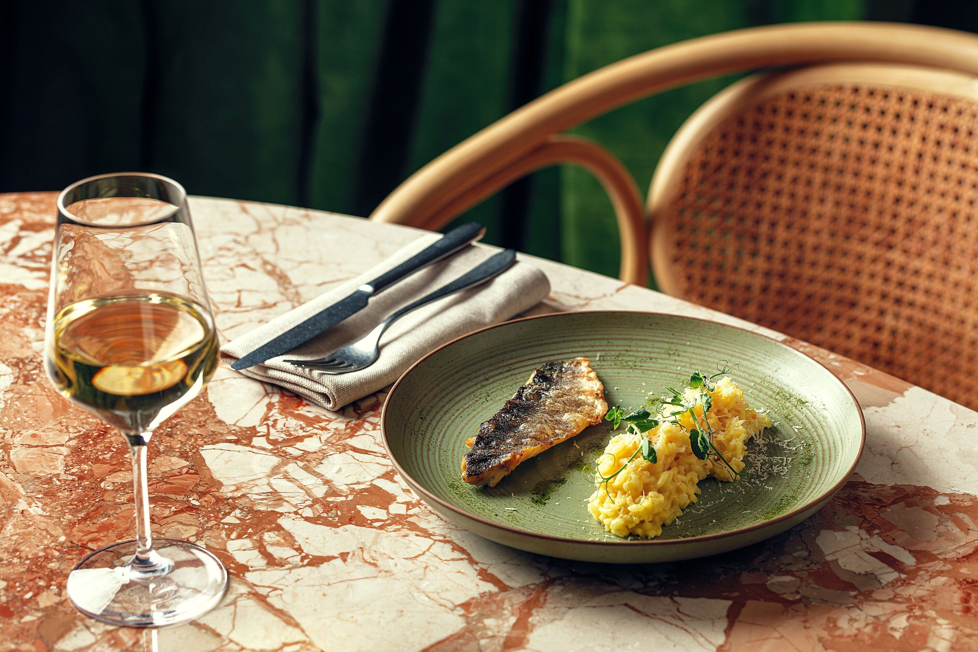 A dining table with a plate of food, a glass of white wine, and cutlery.