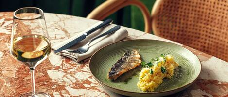 A dining table with a plate of food, a glass of white wine, and cutlery.