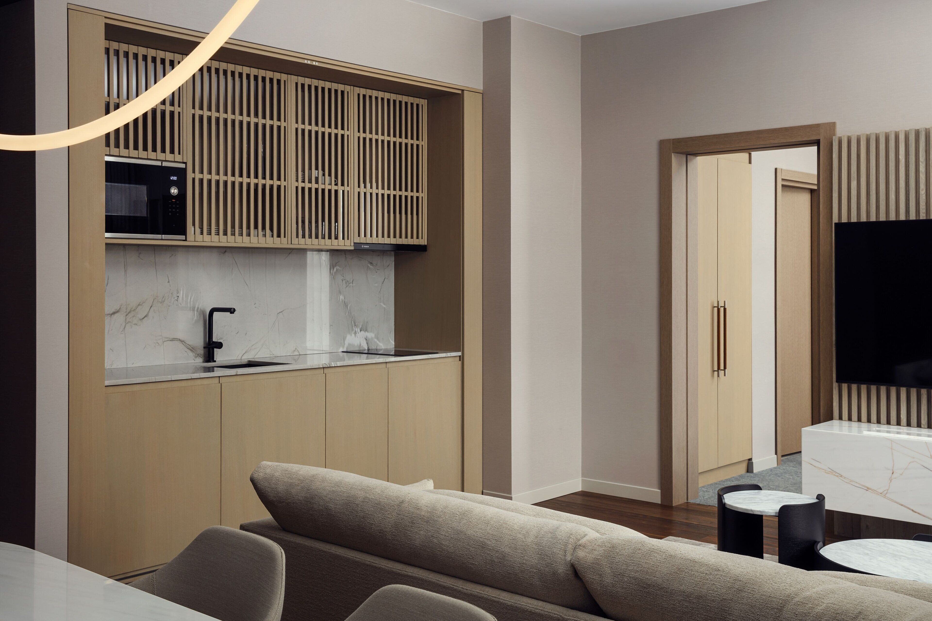 A modern kitchen with a built-in microwave, a sink, and wooden cabinets. There is a seating area with a sofa and a small table.