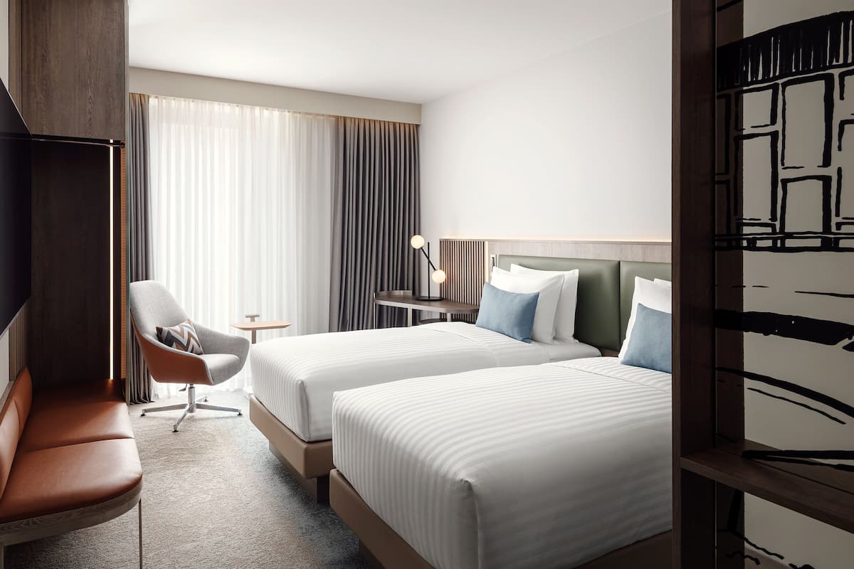 A hotel room with two beds, a seating area, a small table, and a lamp.