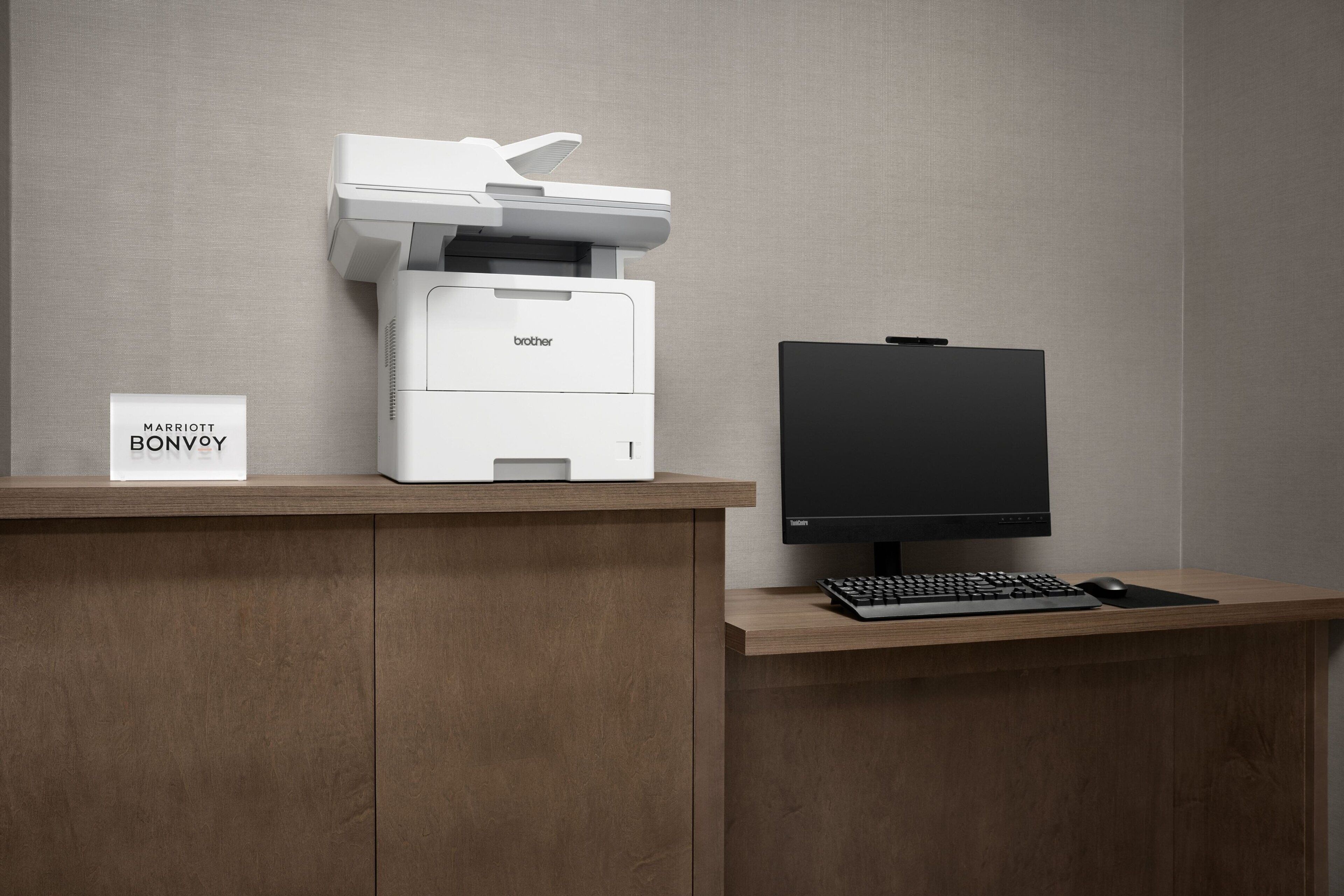 A modern hotel reception desk with a Brother printer, a sign reading "MARRIOTT BONVOY," and a computer monitor.