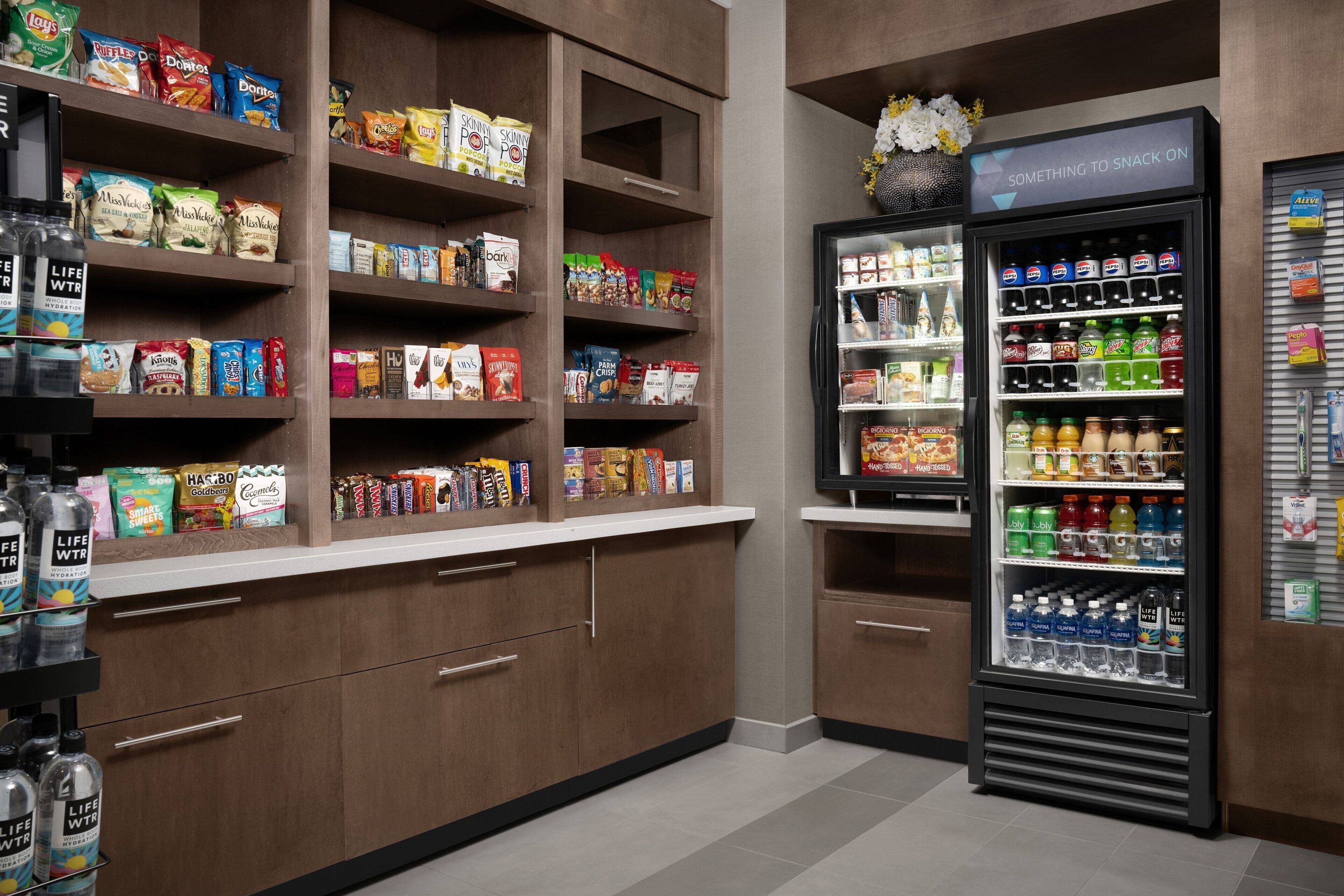 Een afdeling met snacks en drankjes, met volgepakte schappen, een koeltoog en een drankenspender.