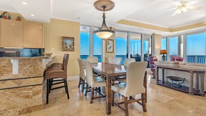 A spacious dining area with a large wooden table and chairs, a kitchen with marble countertops, and a view of the ocean through large windows. - La Playa 1001 (Pensacola)