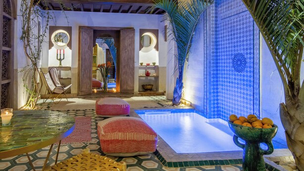 Un espacio interior bien iluminado con piscina, zonas de estar y elementos decorativos como plantas y un bol de naranjas.