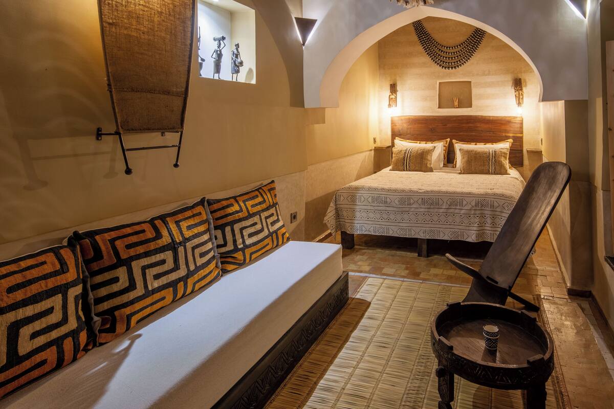 A bedroom with a bed, a sofa, a wooden chair, and a small table.