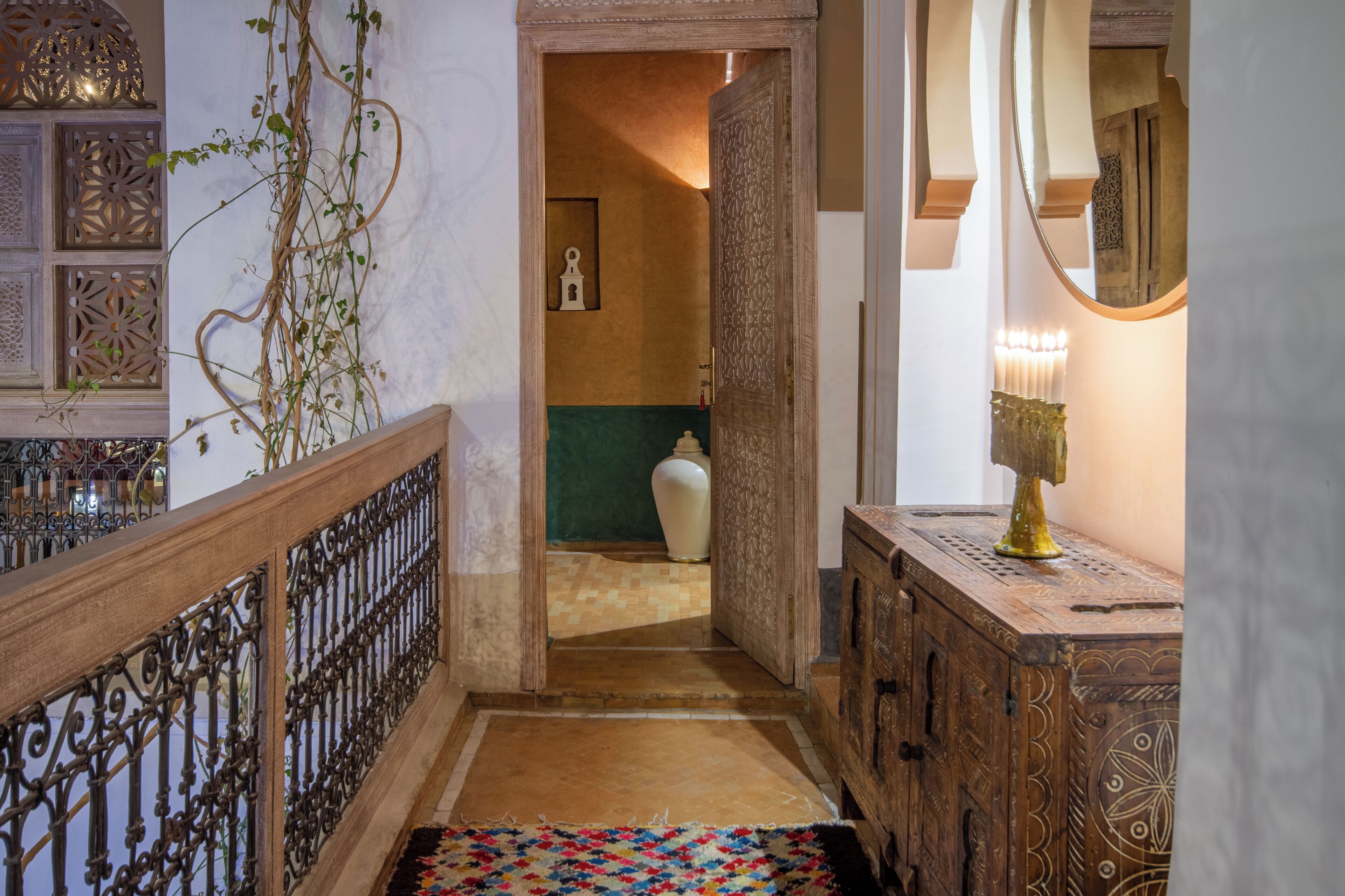 A hallway with a patterned rug, a wooden railing, a decorative vase, and a mirror on a wooden cabinet.