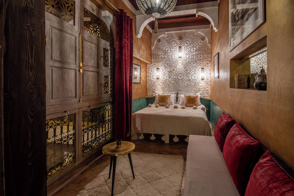 A room with a bed, a red sofa, a small round table, and a decorative wall.