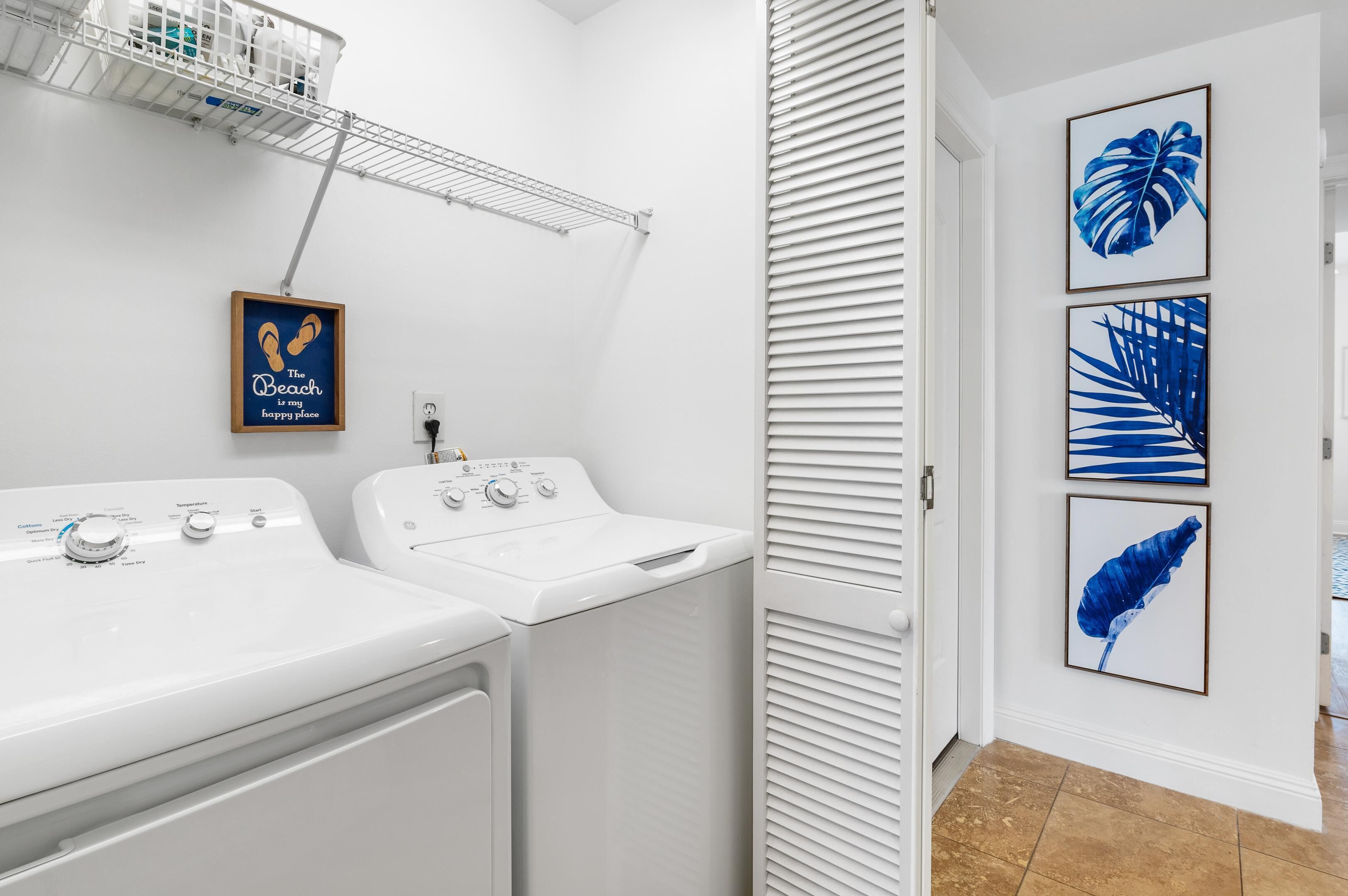 A laundry area with two white washing machines, a drying rack, and a framed quote on the wall.