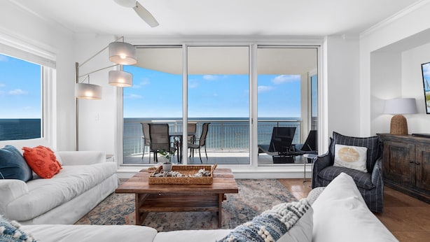 A spacious living room with a large window overlooking the ocean, a ceiling fan, and a cozy seating area with a coffee table. - Indigo West 1101 (Pensacola)