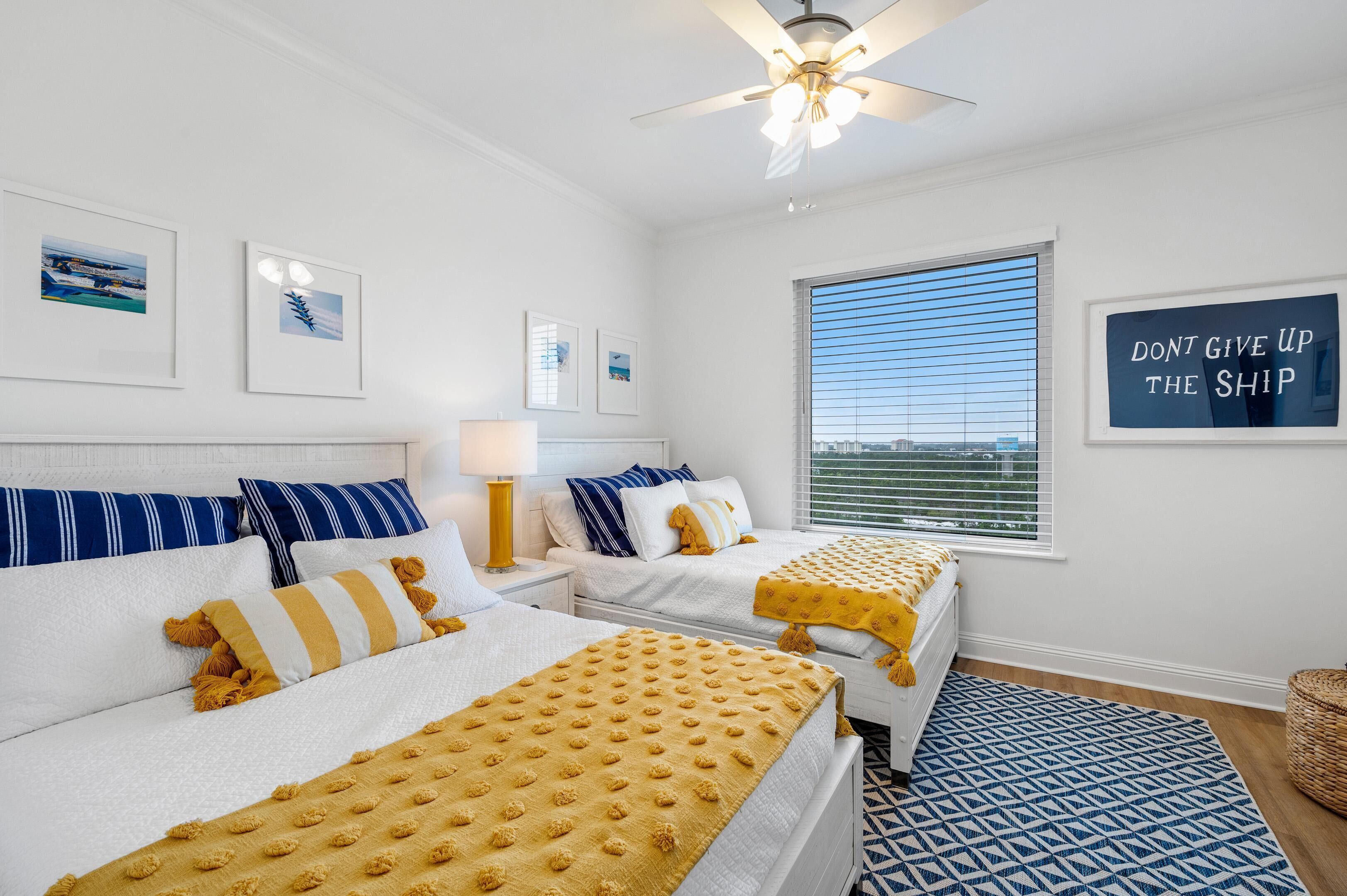A hotel room with two beds, a ceiling fan, a window with blinds, and a motivational sign on the wall.