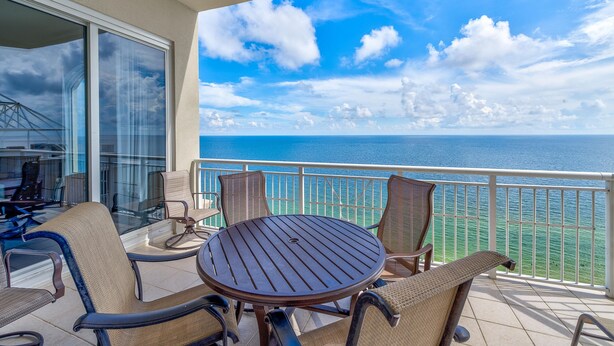 Un balcone con un tavolo rotondo e sedie, con vista su un mare e un cielo azzurri.