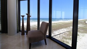 A room with a large window offering a view of the beach and ocean. There is a chair and two tall, slender floor lamps. - Capri 302 (Pensacola)