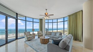 A spacious living room with a large window overlooking a beach, furnished with a sofa, chairs, and a coffee table. - Capri 302 (Pensacola)