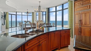 A spacious kitchen with a large island, wooden cabinets, and a view of the ocean. - Capri 302 (Pensacola)