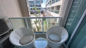 A balcony with two white wicker chairs and a small table, overlooking a modern building complex. - Brisas do Lago - Apartamento 12 (Brasília)
