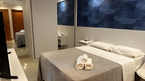 A hotel room with a bed, a bedside table, a nightstand, a mirror, and a wall with a geometric pattern. - Brisas do Lago - Apartamento 12 (Brasília)