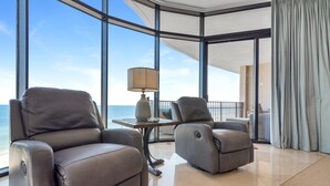 A modern lounge area with leather recliners, a table with a lamp, and a view of the ocean through large windows. - Capri 601 (Pensacola)