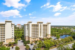 Surrounded by lush greenery and a body of water, this residential building offers a serene environment with balconies on each floor.