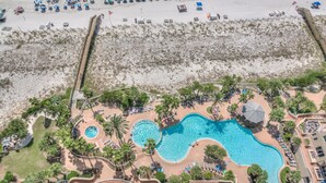 An aerial view of a resort with a large swimming pool, beach area, and various amenities.