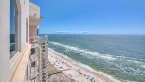 A high-rise building with a balcony overlooking a beach with umbrellas and sun loungers.