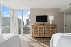 A hotel room with two beds, a large window with curtains, a TV on a wooden cabinet, and a lamp. - Perdido Sun 616 (Pensacola)