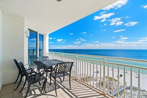 A balcony with a table and chairs, overlooking a beach with clear skies and calm waters. - Seaspray East 924- Gulf Front (Pensacola)